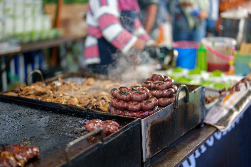 In a close-up shot, an Asian market vendor is captured preparing pan-fried meat, showcasing the sizzling and flavorful cooking process.