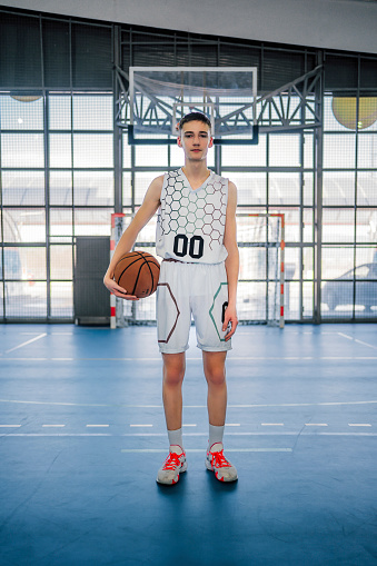 Teenager boy holding professional basket ball over isolated pink background with a happy face standing and smiling with a confident smile showing teeth