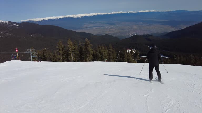 Male skier dressed in black, man skiing down a tree lined snowy mountain piste or slope on fresh snow