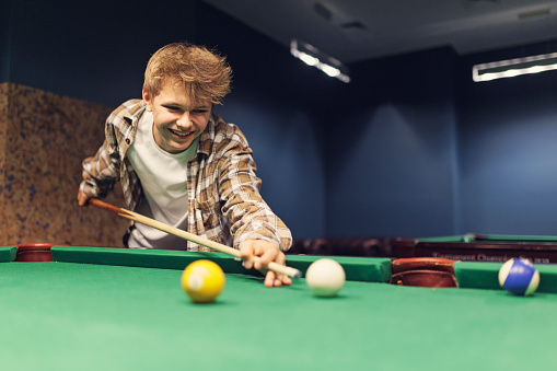 Teenage boy learning to play snooker (billard) at a pub.\nShot with Canon R5