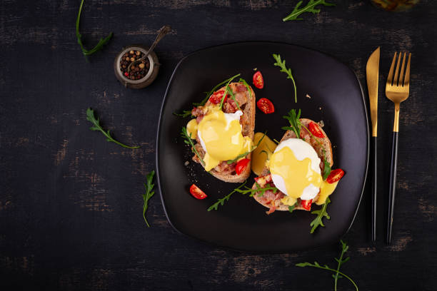 istock Breakfast. Sandwich with ham, poached egg, onion and arugula in a plate on a dark background. Top view 1947410276