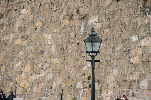 Varberg, Sweden - April 01 2023: Street lamp by a tall stone wall.