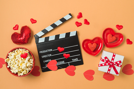 Happy Valentine's day and romantic movie concept with  movie clapper board, heart shapes and popcorn on trendy background. Top view, flat lay