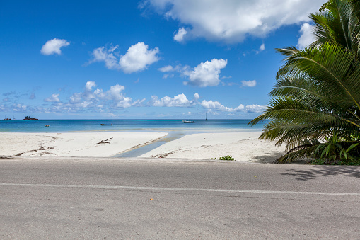 asphalt road and white sand beach at praslin island, seychelles islands, indian ocean islands.