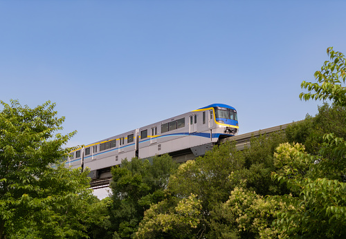 Osaka, Japan - July 6 2023: Osaka Monorail vehicle with blue and yellow colors, running in trees