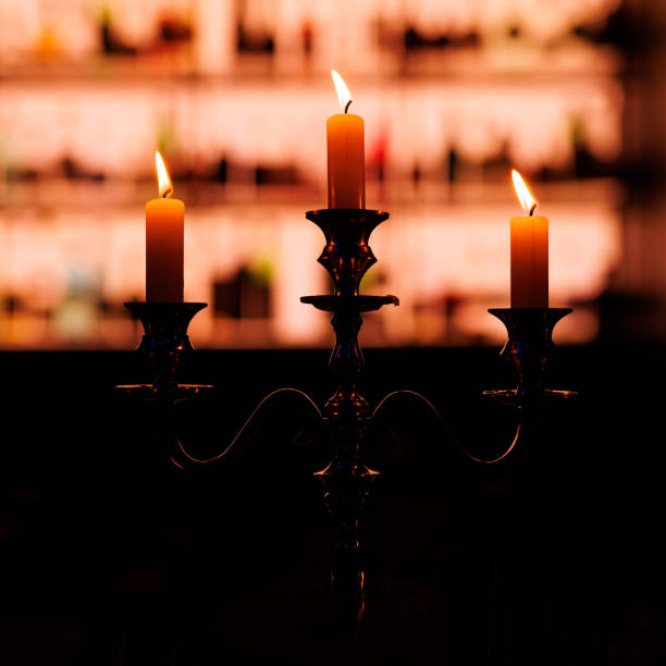 istock A vintage candelabra with three lit candles casts a warm glow, silhouetted against a backdrop of illuminated shelves 1947470585