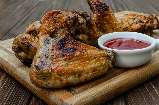 Grilled chicken wings with ketchup on a wooden board. Traditional baked barbecue