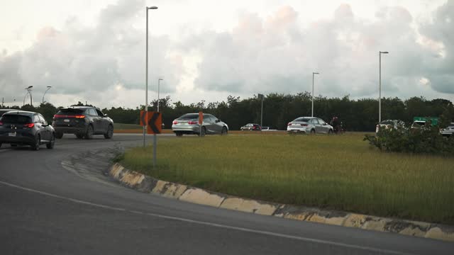 Many cars entering a roundabout on the multi lane road at rush hour at sunset. People returning home from work at the end of the day.