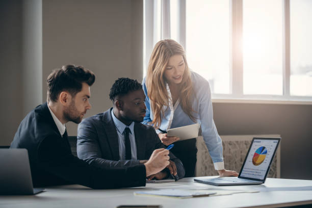 istock Three business people in formalwear analyzing diagram on laptop while working in office together 1947497636