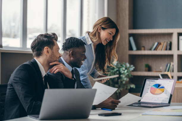 istock Three smiling business people analyzing charts and using laptop while working in the office together 1947497640