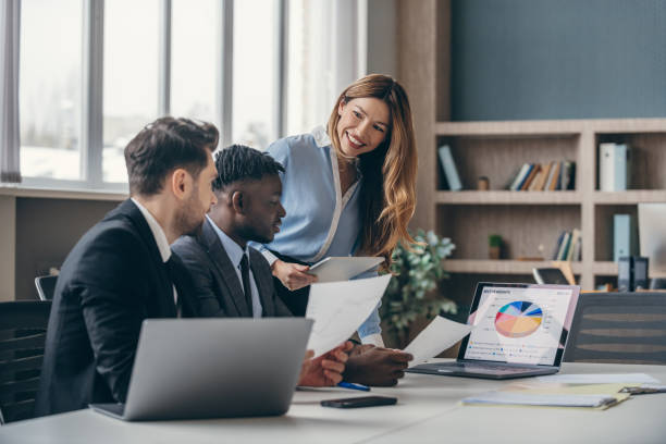 istock Three smiling business people analyzing charts and using laptop while working in the office together 1947497651