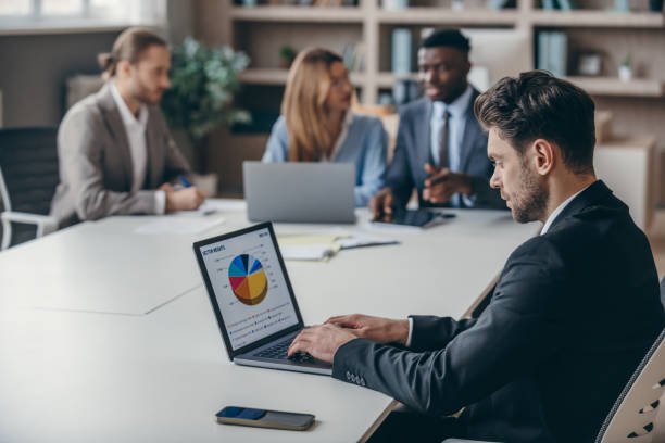 istock Confident businessman analyzing chart on laptop while his colleagues working together on background 1947498291