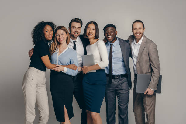 istock Smiling young business team in formalwear embracing while standing on beige background 1947507597