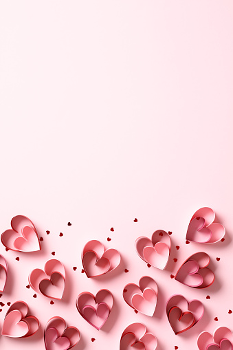 Red paper cut hearts and confetti on pink background. Happy Valentines Day vertical background.