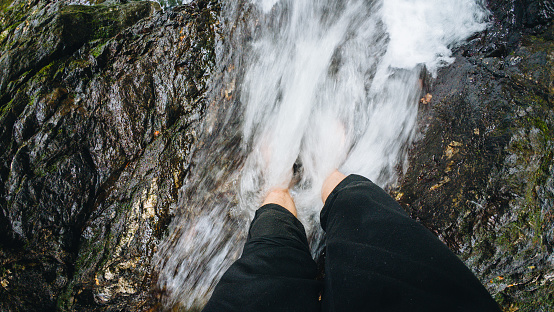 young man's feet over a waterhole of a waterfall in a forest with trees on vacation