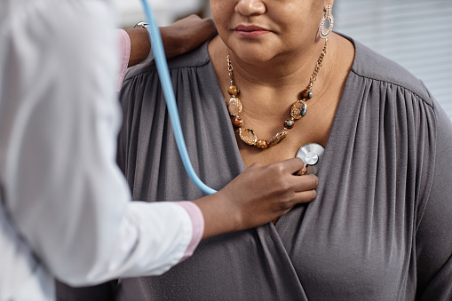 Cropped shot of unrecognizable female patient at check up in clinic with doctor pressing stethoscope to her chest