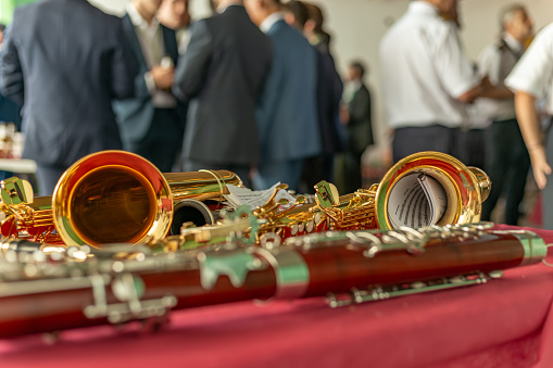 Castilla La Mancha, Spain. Close-up of wind instruments on a table. In the background, local authorities and members of the town's music band during the patron saint festival season.