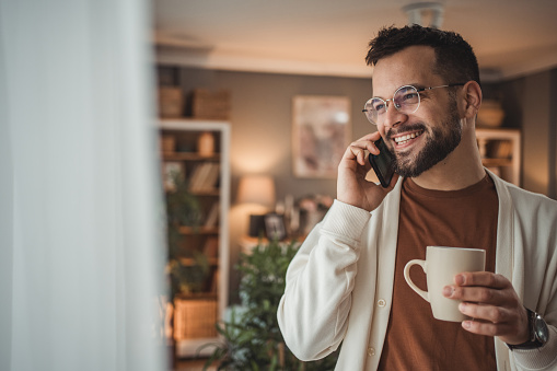 Portrait of a handsome Caucasian man standing by the window with a cup of coffee in his home