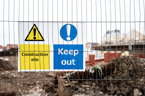 Shallow focus of health and safety construction signs seen on a metal barrier at an affordable homes housing site.