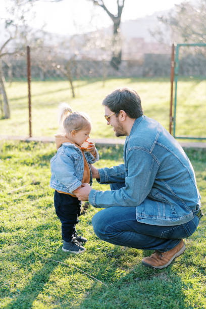istock Dad squatted next to a little girl eating an apple on a green meadow 1947634382