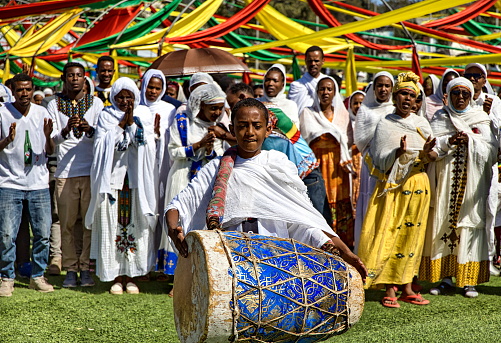 Addis Ababa, Ethiopia - January 19, 2023: Choir of men and women perform hymns during Timkat celebrations and a boy is playing the drum. \nTimket is an Ethiopian Orthodox Tewahedo Church celebration of Epiphany. It is celebrated on 19 January (or 20 in a leap year), corresponding to the 11th day of Terr in the Ge'ez calendar. On this day, crowds assemble together with priests who are carrying over their heads covered replicas of the \