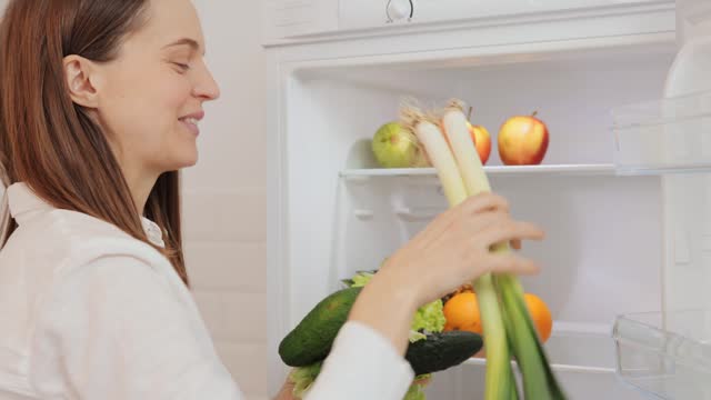 Happy cheerful woman enjoying healthy nutrition taking fresh vegetables from fridge for cooking diet veggies dinner taking products from refrigerator for preparing tasty breakfast