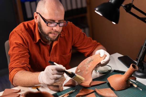 istock Male archaeologist dig ancient pottery object working in archaeological office at night. 1947648058
