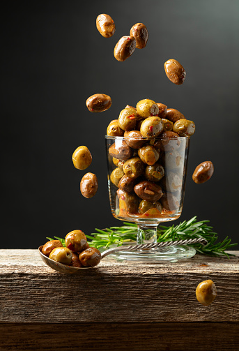 Spicy olives in a glass bowl. Bowl with preserved olives and rosemary twigs on a wooden table.