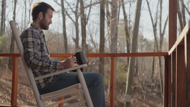 Young man sitting on front porch reading his Bible and drinking coffee