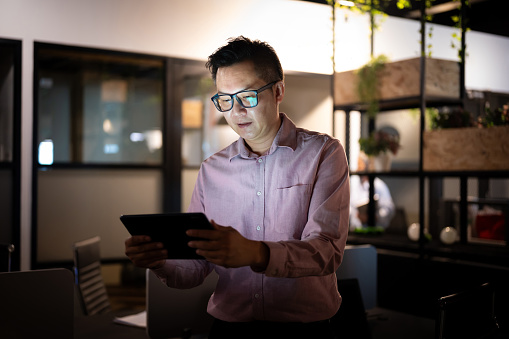 Mature male business entrepreneur checking his investment online using smart phone at his workstation.