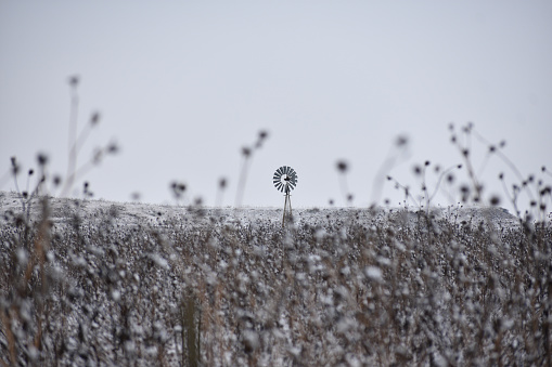 A vintage windmill is depicted standing alone in a desolate winter landscape