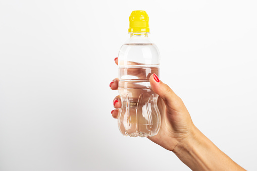 Transparent plastic bottle with fresh water in a female hand on a white background. Space for text.