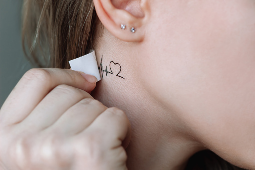 A young woman applying a temporary mini tattoo in the form of a heart and a cardiogram on her neck