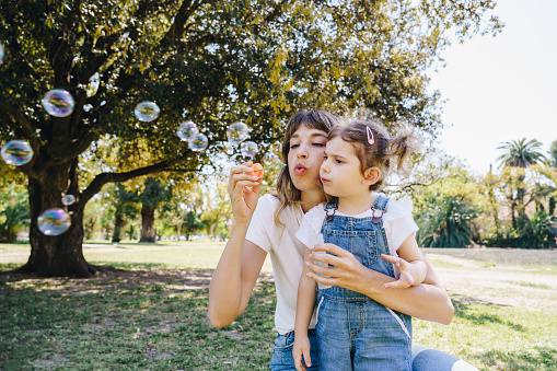 Mother and daughter having fun blowing soap bubbles at the park