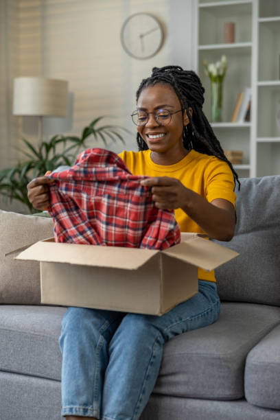 istock Smiling dark-skinned woman opening box with clothes and looking contented 1947829633