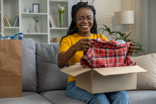 istock Young woman taking a checkered shirt from the box and smiling 1947830143