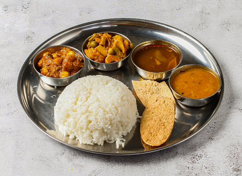 Vegetable thali set with plain rice, palak, dal, mixed vegetable of aloo gobi matar, dal, palak nachos, and shorba served in dish isolated on background top view of indian spicy food