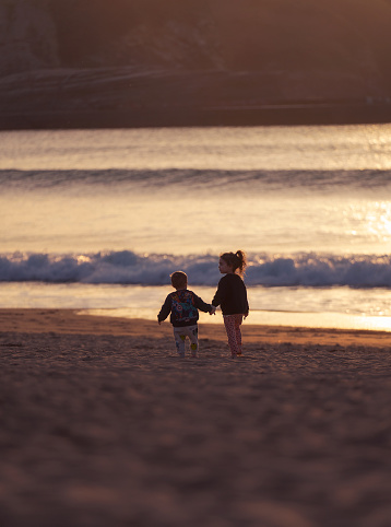 2 children walking along the beach during the sunset