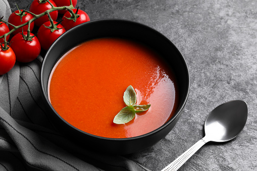 Delicious tomato cream soup in bowl served on dark textured table, closeup