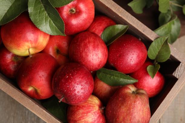 istock Crate with wet red apples and green leaves on table, top view 1947968802