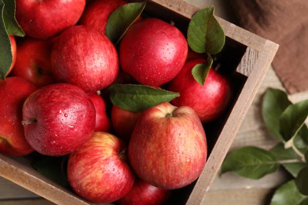 istock Crate with wet red apples and green leaves on table, top view 1947968804
