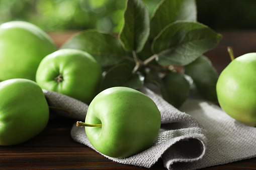 Fresh ripe green apples and leaves on wooden table outdoors, closeup