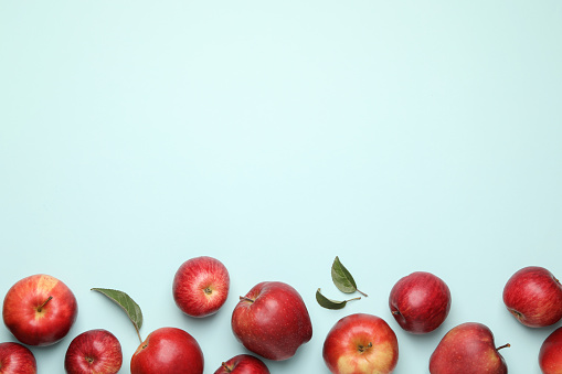 Fresh red apples and leaves on light blue background, flat lay. Space for text