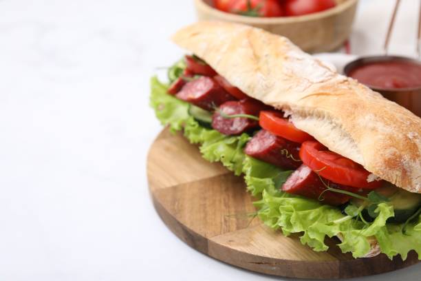 istock Delicious sandwich with sausages and vegetables on white table, closeup. Space for text 1947982967