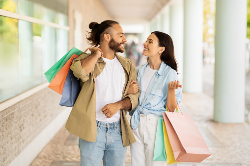 Satisfied millennial caucasian lady and guy shopaholics with many packages, enjoy shopping together, new clothes smile in mall. Walk, sale and relationships, discount, fun and love