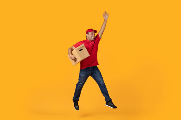 istock Hispanic Young Courier Man Jumping Holding Cardboard Box, Yellow Background 1948033312