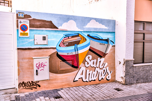 Bogota, Colombia - May 28, 2018: A local Colombian man walks through a colorful street in the historic La Candelaria District in the capital city of Bogota in the South American country of Colombia, quite unmindful of the brightly painted walls. Many of the street facing walls in the area are painted in the vibrant colours of Colombia, sometimes depicting Pre-Colombian legends or modern Street Art and Graffiti. The mural in the backgound, to the left was done by the popular Colombian Street Artist called Rodez. Some Graffiti touts have unfortunately defaced the mural by signing over it. Photo shot in the late afternoon sunlight in the Golden Hour; horizontal format. Camera: Canon EOS 5D MII. Lens: Canon EF 24-70mm F2.8L USM.