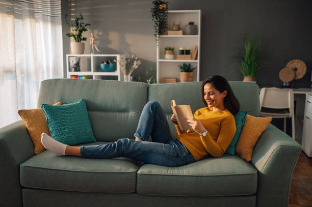 istock Young woman lying on comfortable sofa reading a book in her free time at home 1948062941