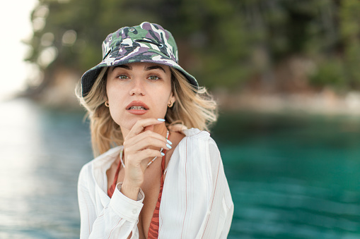 A beautiful young blond woman with a hat standing on a sailboat, looking at camera