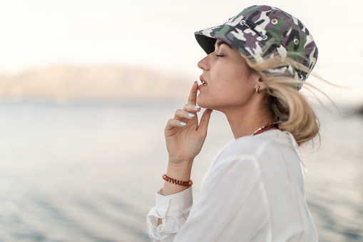 A beautiful young blond woman with a hat standing on a sailboat, her eyes are closed, she is enjoying the moment.